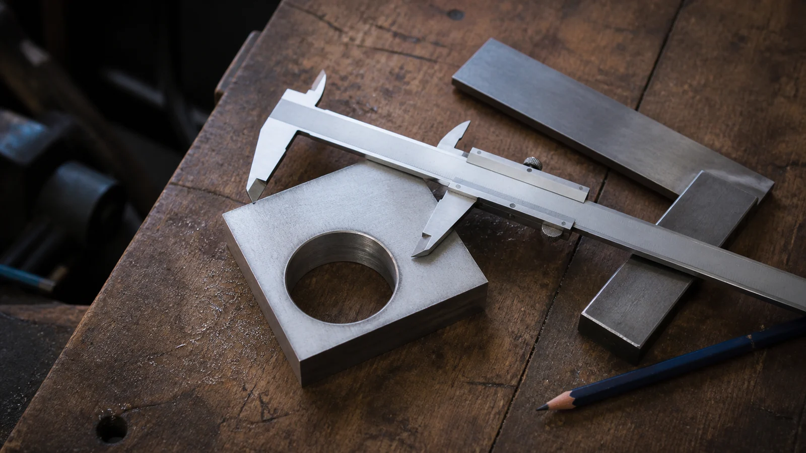 A metal caliper laid across a machined steel part on a worn wooden workbench